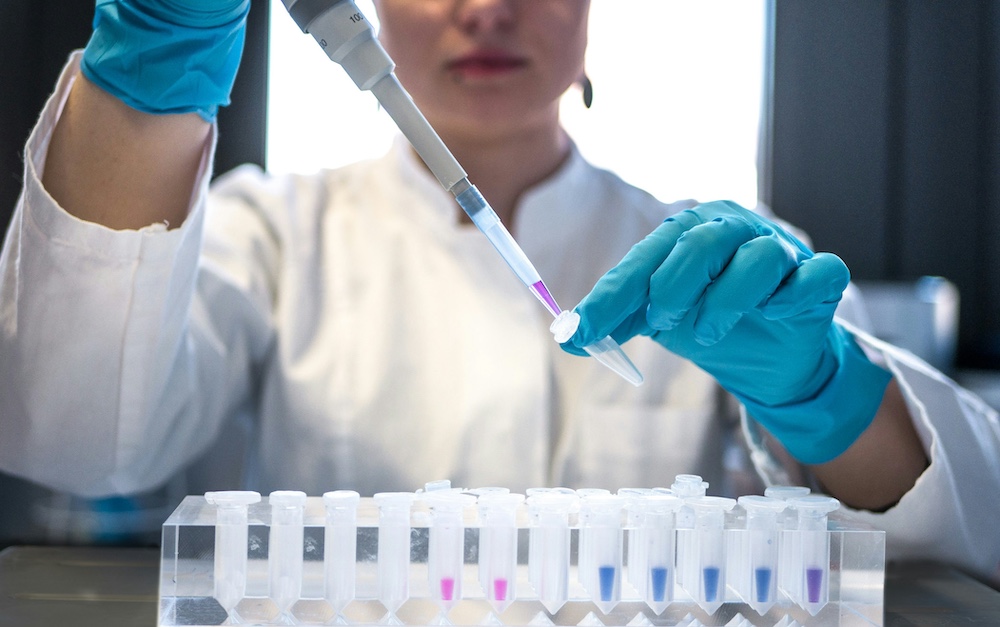 Scientist in a lab coat pipetting a colored sample into a rack of microtubes during bioavailability testing